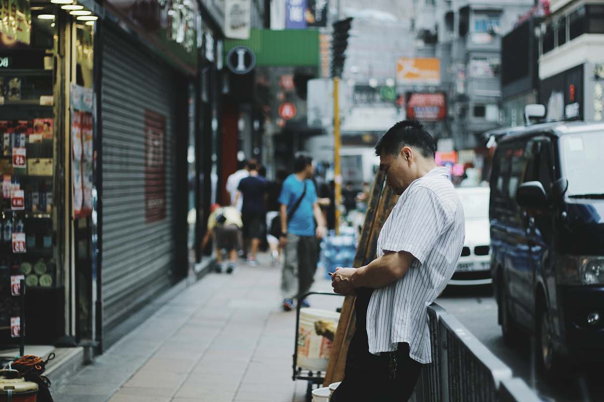 hong kong shallow photography of man leaning towards grey steel fence shop